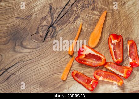 Große fleischige rote Paprika und in Scheiben geschnittene Karotten werden auf die Ecke eines natürlichen Holztisches gestellt. Kopierbereich Stockfoto
