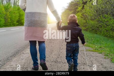 Morgenspaziergang. Das Kind mit seiner Mutter geht auf der Straße zum Sonnenaufgang. Stockfoto