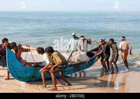 Fischer schleppen ihr traditionelles Holzboot vom Meer am Marari Beach nach einem frühmorgendlichen Angelausflug. Kerala, Indien Stockfoto