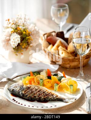 Ein Teller mit gegrilltem Fisch, serviert mit gekochtem Gemüse und Orangenscheiben Stockfoto