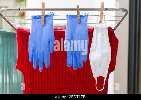 Hausgemachte Gesichtsmaske und Gummihandschuhe hängen an einer tragbaren Wäscheleine. Foto, das zeigt, dass das Schutzmaterial gegen Kovid-19 wiederverwendet werden muss Stockfoto