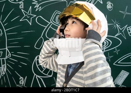 Trägt einen Helm von Astronauten kleinen Jungen vor der Tafel stehen Stockfoto