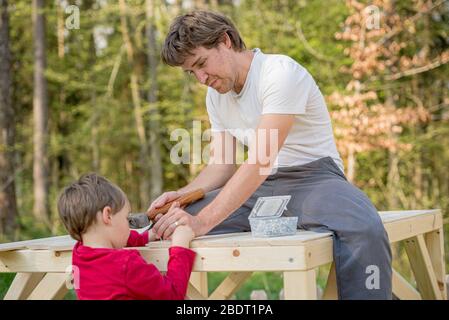 Junger Vater baut Holzspielhaus mit seinem Kleinkind Sohn draußen im Hinterhof. Stockfoto