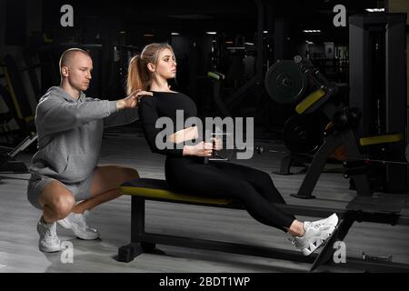 Attraktives Mädchen mit einem Personal Trainer, der in einem Fitnessstudio arbeitet. Fitnesstrainer führt persönliches Training durch. Stockfoto