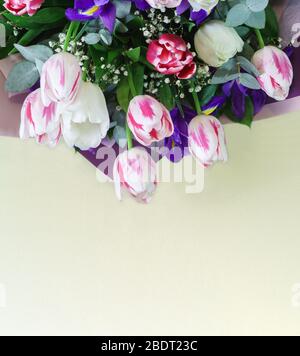 Ein leuchtendes Frühlingsbouquet mit Tulpen und Iris in Papierverpackung liegt auf einem gelben Tisch. Kopierbereich Stockfoto