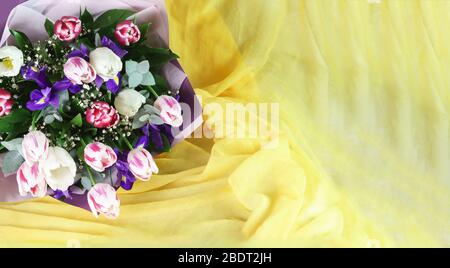 Leuchtendes Frühlingsbouquet mit Tulpen und Iris in einer Geschenkbox und einem gelben Taschentuch. Kopierbereich Stockfoto