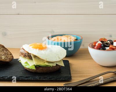 Vegetarischer Cheeseburger mit Tomaten, Oliven und Feta-Salat sowie Fenchel- und Karotten-Salat. Stockfoto