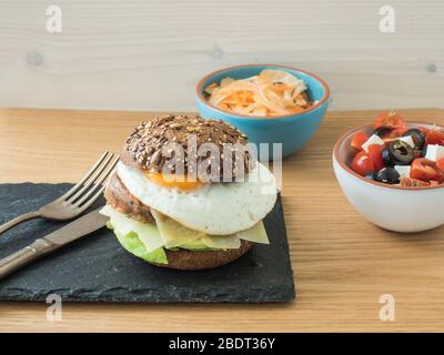 Vegetarischer Cheeseburger mit Tomaten, Oliven und Feta-Salat sowie Fenchel- und Karotten-Salat. Stockfoto