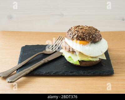 Vegetarischer Cheeseburger, Vintage-Messer und Gabel auf einem Schieferteller Stockfoto