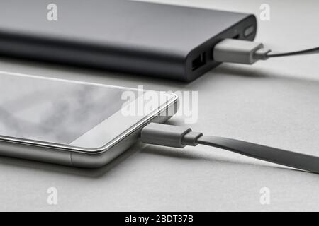 Das Smartphone wird über ein Kabel von einer externen Powerbank geladen. Weißer Hintergrund, Nahaufnahme, selektiver Fokus Stockfoto