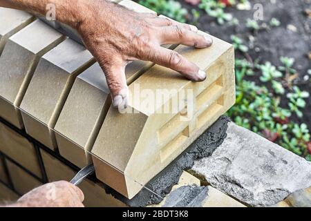 Maurer, der Steine auf den neuen Zaun von den verkleidenen Ziegel installiert. Stockfoto