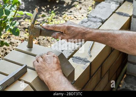 Maurer, der Steine auf den neuen Zaun von den verkleidenen Ziegel mit Hammer installiert. Stockfoto