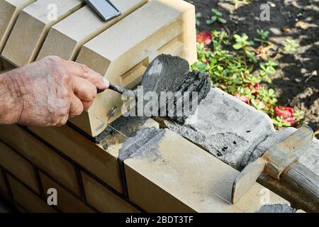 Maurer, der Steine auf den neuen Zaun von den verkleidenen Ziegel mit dem Kitt Messer installiert. Stockfoto