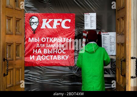 Moskau, Russland. April 2020. Ein Kurier des Lebensmittelzulieferdienstes "Delivery Club" kauft während der Novelkoronavirus COVID-19-Epidemie in Russland im KFC-Restaurant auf dem Komsomolskaya-Platz im Zentrum Moskaus Lebensmittel ein. Auf dem Banner vor dem KFC-Restaurant steht: "Wir sind offen zum Mitnehmen". KFC änderte das Firmenlogo und fügte eine medizinische Maske hinzu Stockfoto