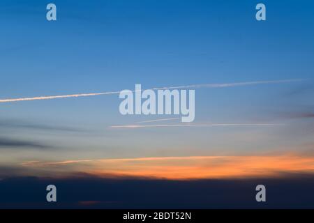 Contrail aus einem Flugzeug auf einem blauen Himmel gegen einen Sonnenuntergang. Stockfoto