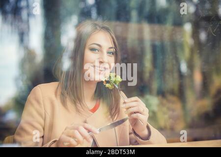 Frau glücklich essen. Nahaufnahme Porträt schön lächelnd toothy Mädchen Student Blick auf Sie Kamera essen grünen Salat Café Hintergrund. Gesund ha Stockfoto