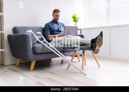 Mann Mit Beinverletzung Auf Sofa Mit Laptop Sitzen Stockfoto