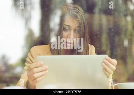 Schockiert Frau halten Computer Laptop Tablet-Bildschirm schauen überrascht in Coffee-shop Stockfoto
