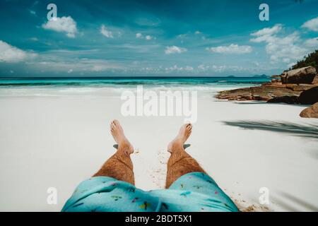 Männer in Badeshorts, die sich auf dem weißen Sandstrand mit wunderschönem Blick auf die Lagune des blauen Ozeans ausruhen. Stockfoto