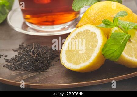 Tasse mit Tee, Zitrone und grünem Blatt auf Holzhintergrund. Stockfoto