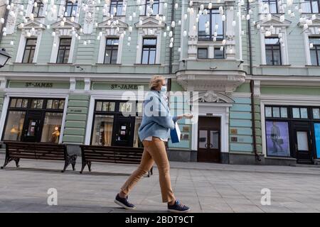 Moskau, Russland. 9. April 2020 EINE Frau mit Gesichtsmaske geht die Stoleshnikov Lane im Zentrum von Moskau während der COVID-19-Pandemie in Russland. Die Straße ist berühmt für ihre Lage Boutiquen und Geschäfte mit vielen Luxusgütern innerhalb des Boulevard Ring im Zentrum von Moskau. Stockfoto