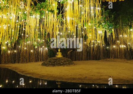 Buddha-Skulptur im Wat Phan Tao unter einem Bodhi-Baum und goldenen Girlanden in Chiang Mai, Thailand. Stockfoto