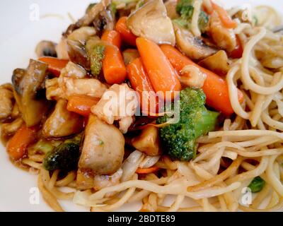 Pasta mit Gemüse, Pilzen und Huhn auf einem weißen Teller. Chinesische Nudeln, gebratenen Soba Nudeln mit Champignons, Möhren, Paprika closeup auf weißen Plat Stockfoto
