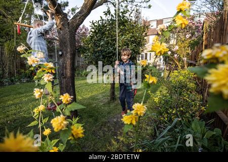 Zwei junge Brüder im Alter von 6 und 9 Jahren spielen auf einer Seilleiter und Seilschaukel in ihrem Garten, London, England, Großbritannien Stockfoto