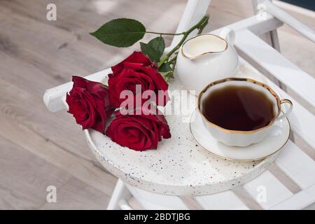 Drei rote Burgunderrosen, eine Tasse Tee und auf einem Tablett. Frühstück. Stockfoto