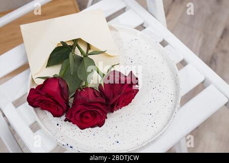Drei rote Burgunder Rosen auf einem Tablett auf dem Stuhl. Kopierbereich Stockfoto