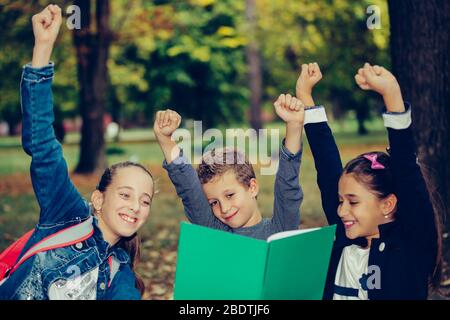 Glückliche kleine Kinder feiern Erfolg mit dem Heben der Hände. Drei glückliche Kinder feiern hervorragende Ergebnisse bei einem Test in der Schule. Selektiver Fokus Stockfoto
