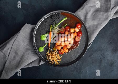 Gegrillte Jakobsmuscheln mit Gemüse und Sauce, eine schöne Präsentation vom Koch, Lebensmittelfoto, dunkler Hintergrund. Kopierraum, Fisch und Meeresfrüchte Stockfoto