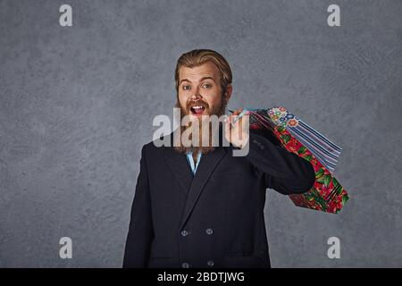 Aufgeregt bärtigen Mann hält Einkaufstaschen isoliert grauen Hintergrund Wand. Stockfoto