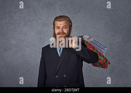 Aufgeregt bärtigen Mann hält Einkaufstaschen isoliert grauen Hintergrund Wand. Stockfoto