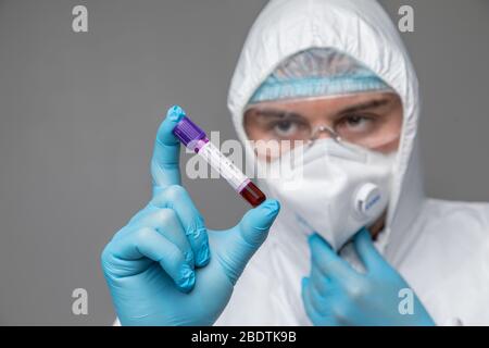 Mann Schutzkleidung Gefahrgut hält Reagenzglas gefüllt mit Blut isoliert auf einem weißen Hintergrund. Stockfoto