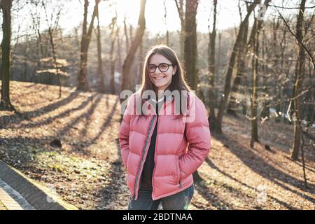 Fröhliches junges Mädchen in einer Brille mit einer rosa Jacke und Jeans Stockfoto