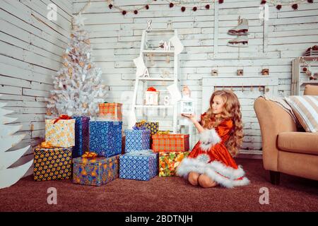 Weihnachten. Elegant in Santa Kostüm Mädchen von 8-9 Jahren mit Freude gekleidet bewundert weißen Weihnachtsbaum Dekoration. Weihnachten - geheimnisvoll und wundersam Stockfoto