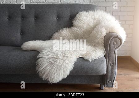 Weiße Schafhaut auf einem grauen Sofa. Ein gemütlicher Ort zum Entspannen in der Wohnung. Moderne Einrichtung im skandinavischen Stil Stockfoto
