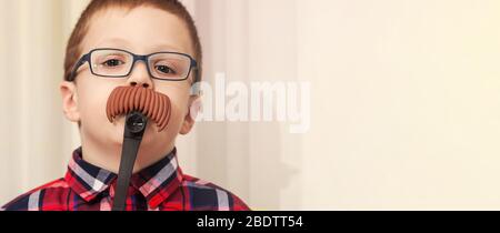 Kleiner Junge in einer Brille mit dekorativem Schnurrbart. Falscher Schnurrbart. Spiel des Erwachsenenlebens. Stockfoto