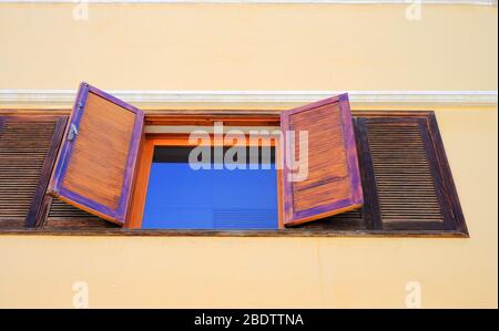 Fensterscheibe, die blauen Himmel reflektiert, breite offene Holzläden, Wand, niedrige Sicht. Stockfoto