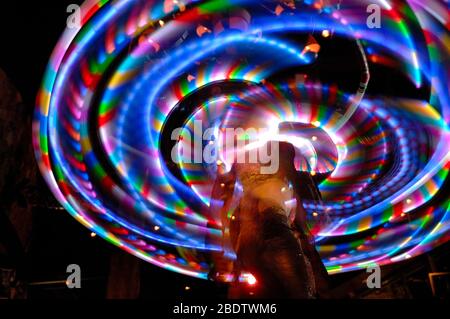 Tänzer mit mehrfarbigem Hula Hoop Reifen aufgenommen mit Slow Shutter Speed, um Bewegung und Weichzeichnung zu zeigen Stockfoto