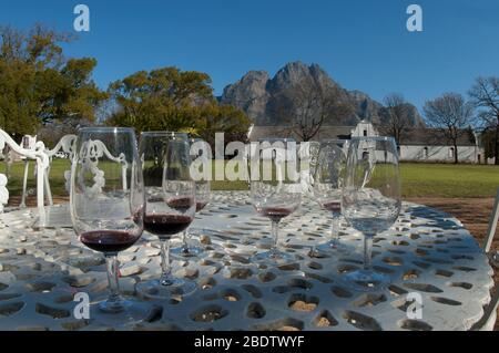 Rotweingläser im Freien Weinverkostungsbereich mit holländischen Häusern im Hintergrund, Boschendal Winery, Franschoek, nahe Kapstadt, Südafrika Stockfoto