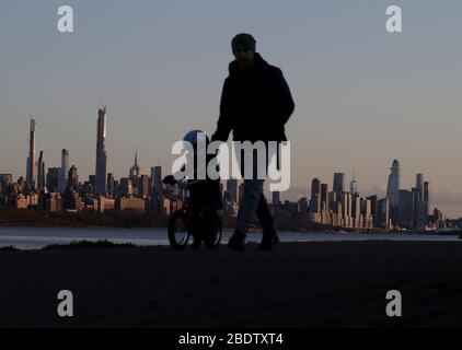 New York, Usa. April 2020. Ein Mann führt ein Kind auf einem Fahrrad, während es auf einem Weg entlang des Hudson River mit Blick auf One World Trade Center und andere Gebäude in der Skyline von Manhattan in New York City am Donnerstag, 9. April 2020. Die Zahl der Todesopfer von COVID-19 in New York City nähert sich 5,000. Foto von John Angelillo/UPI Quelle: UPI/Alamy Live News Stockfoto