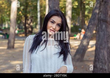 Porträt von glücklichen indischen zuversichtlich junge Frau Blick auf Kamera mit dunklen langen Haaren isoliert grünen Bäumen Park Hintergrund Stockfoto