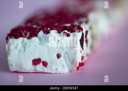 Torrone oder Nougat Bar mit Nüssen und roten getrockneten Beeren. Traditionelles italienisches Dessert auf pinkfarbenem Hintergrund. Süße, leckere und gesunde Speisen Stockfoto