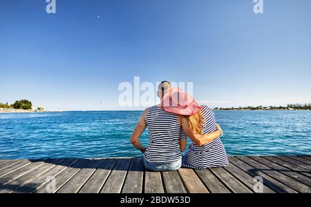 Romantisches Paar in gestreiften Kleid sitzt auf Pier und Suchen im Blue Lake Issyk Kul in Kirgisistan Stockfoto