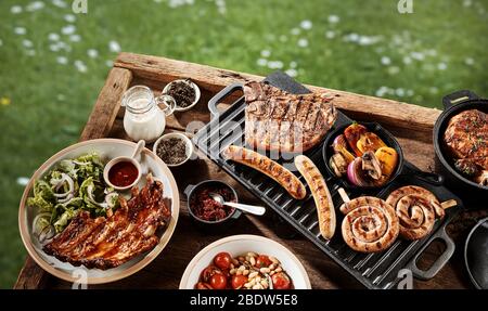 Köstliche Auswahl an gegrilltem Fleisch auf einem Grill auf einem hölzernen Picknicktisch in einem Park oder Garten von oben nach unten gesehen angeordnet Stockfoto