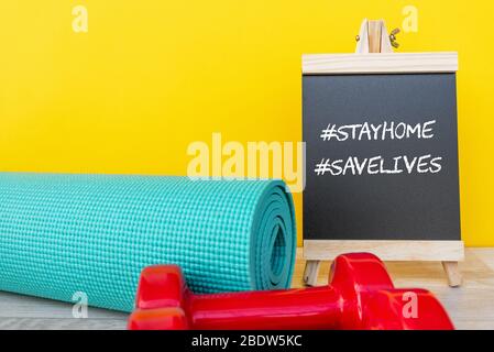 Tafel mit Worten #Zuhause bleiben #Leben retten und Yogamatte und rosa Hantel - Corona Virus Covid - 19 Lock down, eingeschränkte Beweglichkeit und Workout exer Stockfoto