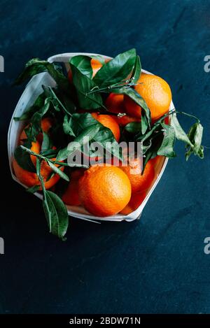 Mandarinen und Apfelsinen, Mandarinen, Clementinen, Zitrusfrüchte mit lgreen Eaves in Korb über rustikal Hintergrund Stockfoto