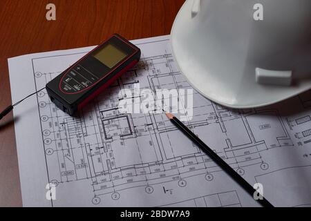 Lasermeter, weißer Hardhat und Zeichnungen am Ingenieurarbeitsplatz. Stockfoto